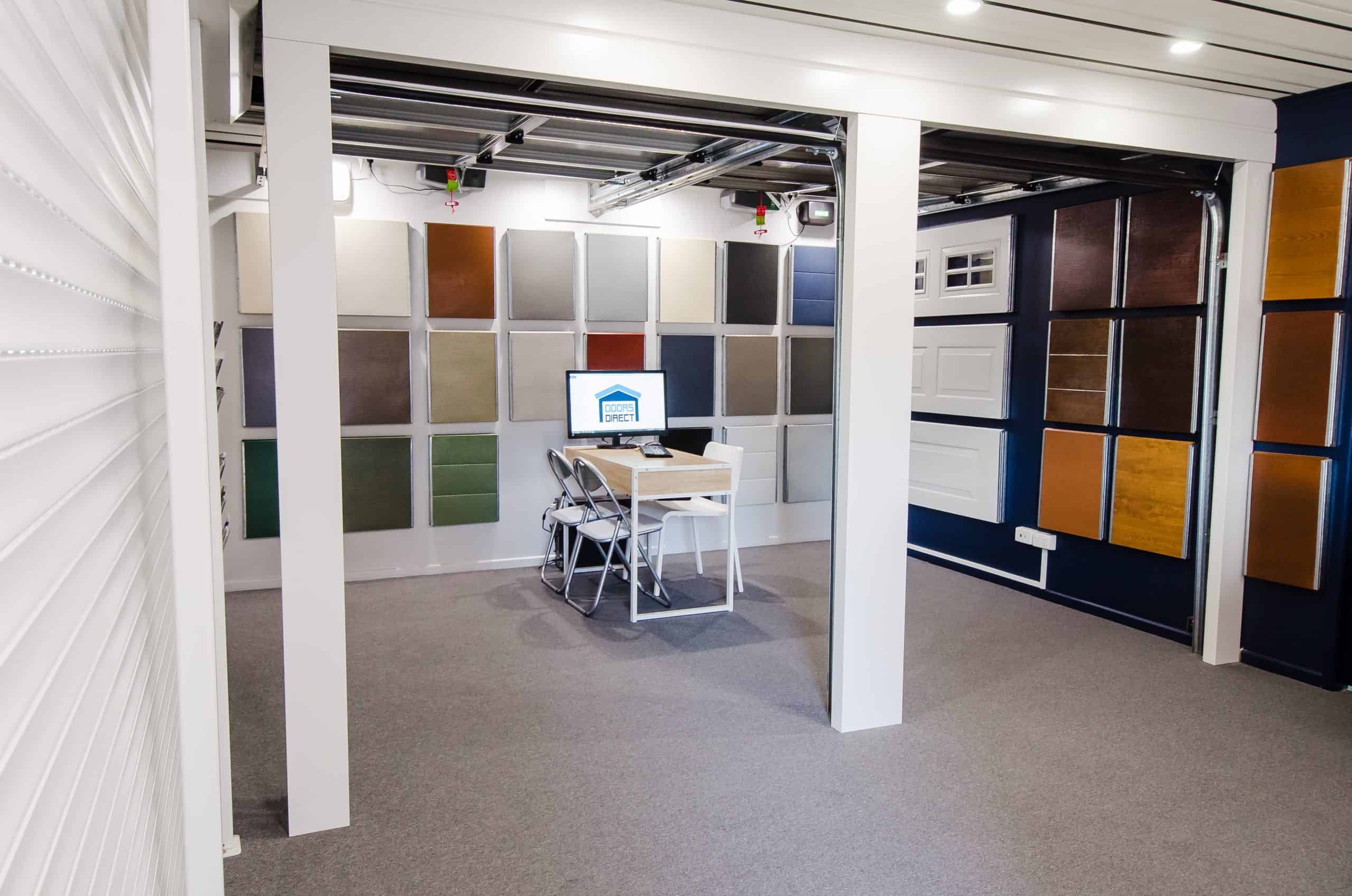 Wide-angle view of a garage door showroom with panel samples, color swatches, and a desk.