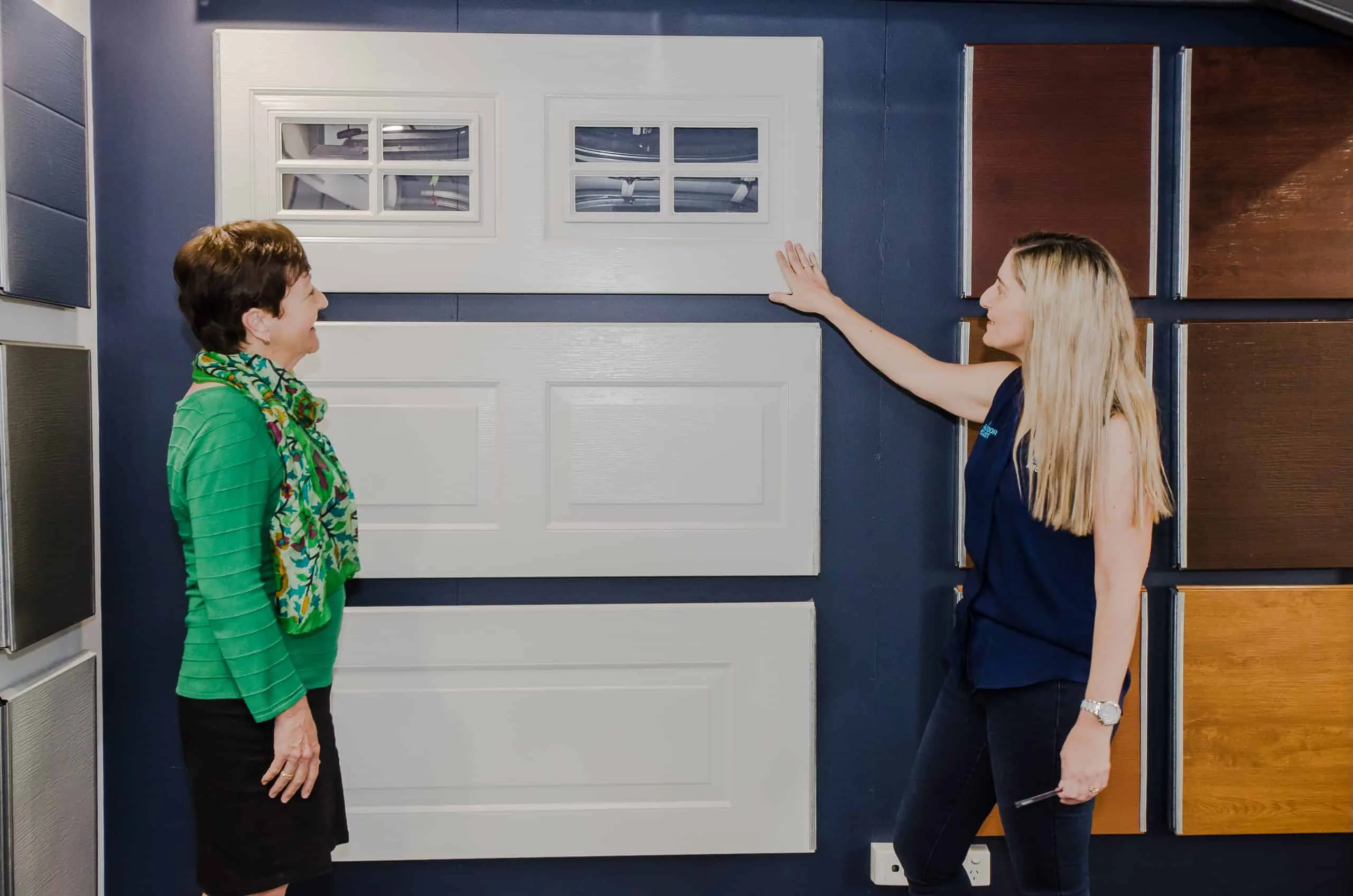 Showroom consultant demonstrating garage door panel samples to a customer in a store setup.
