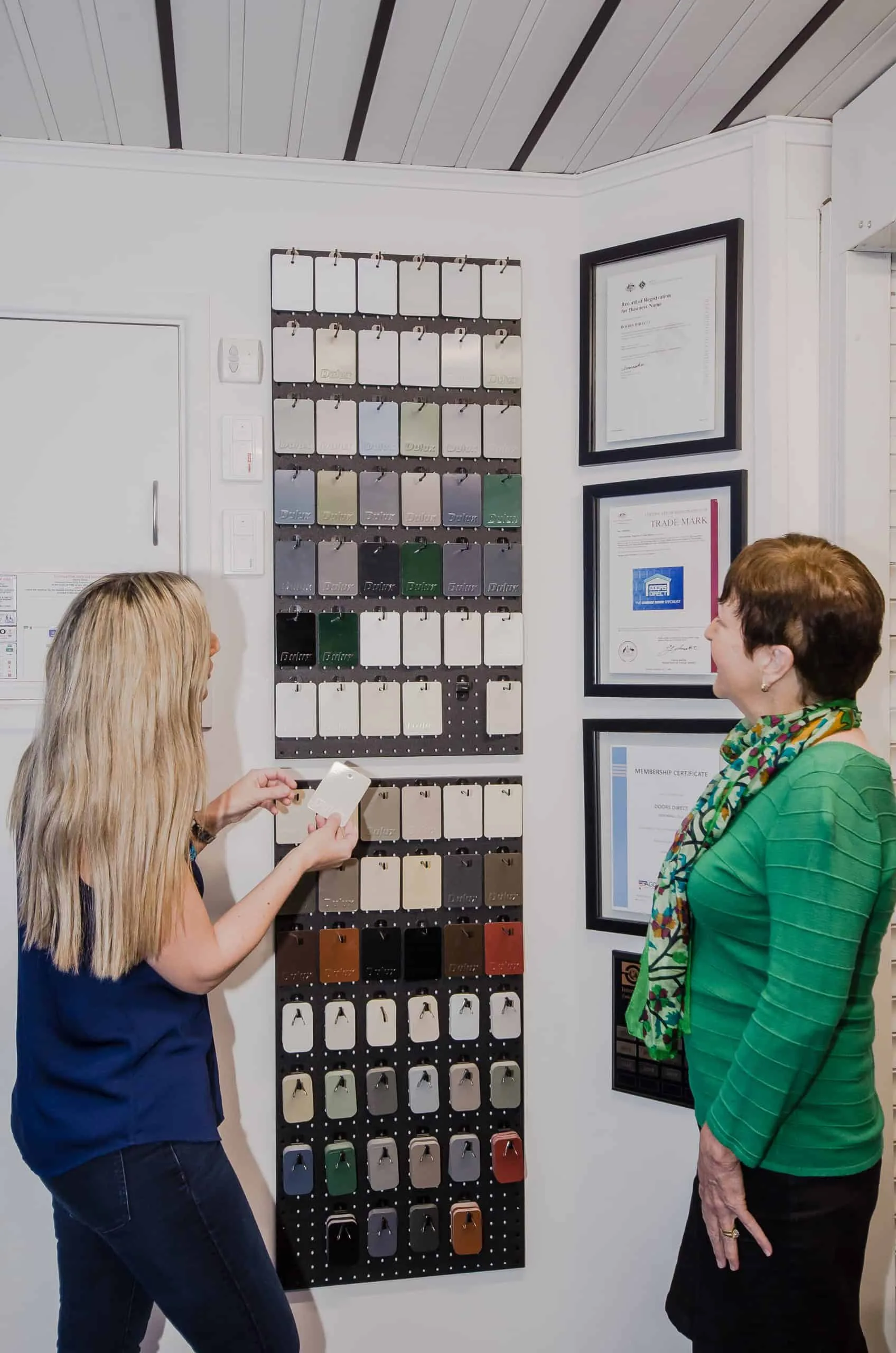 Showroom consultant helping a customer select garage door color samples from a pegboard display.