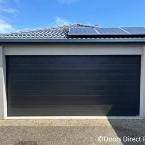 Modern dark grey sectional garage door installed on a suburban house with roof solar panels.
